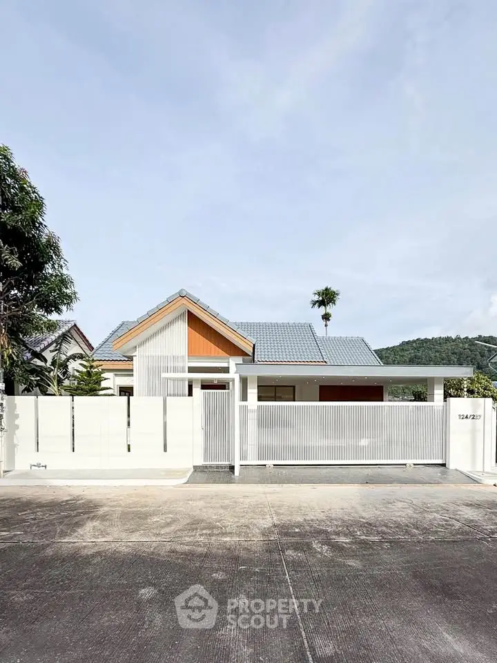 Modern single-story house with sleek design and gated entrance, surrounded by lush greenery and mountain views.