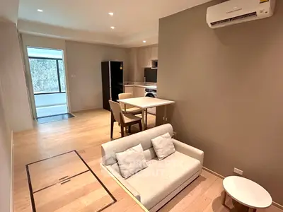 Modern open-plan living room with compact kitchen and dining area, featuring sleek furniture and wooden flooring.