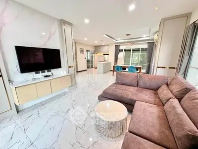 Spacious modern living room with plush sofa and wall-mounted TV, open to elegant kitchen area.
