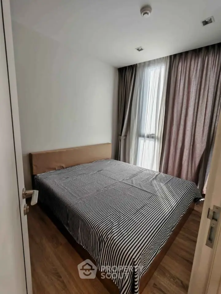 Cozy bedroom with striped bedding and large window with curtains, perfect for relaxation.