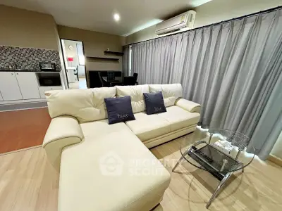 Spacious living room with modern sofa and glass coffee table, featuring elegant curtains and open kitchen layout.