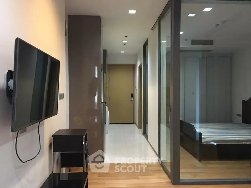Modern apartment interior with glass-walled bedroom and wall-mounted TV