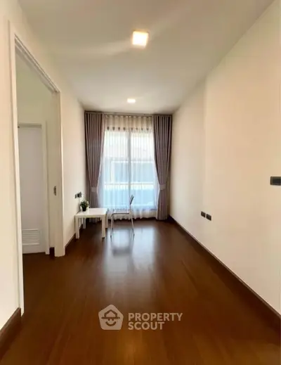 Spacious empty room with wooden flooring and large window, perfect for customization.