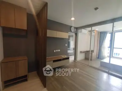 Modern apartment interior with wooden flooring and built-in storage, featuring a sliding glass door to a bright balcony.