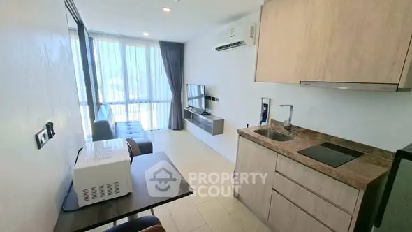Modern studio apartment with kitchenette and living area, featuring large windows and natural light.
