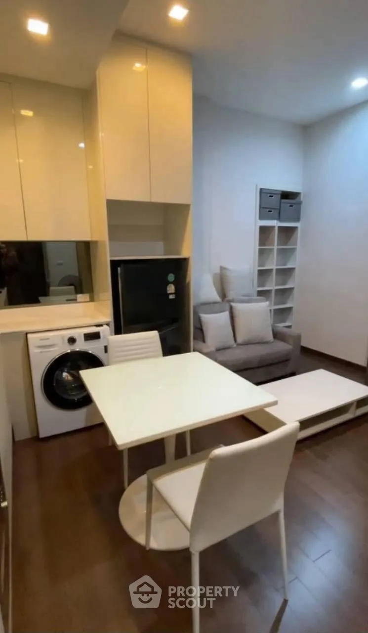 Modern compact living room with integrated kitchen and laundry area, featuring sleek furniture and storage solutions.