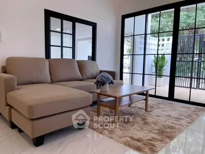 Spacious living room with modern sofa and large windows overlooking greenery.