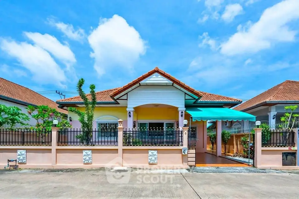 Charming single-story house with tiled roof and fenced yard under a bright blue sky.