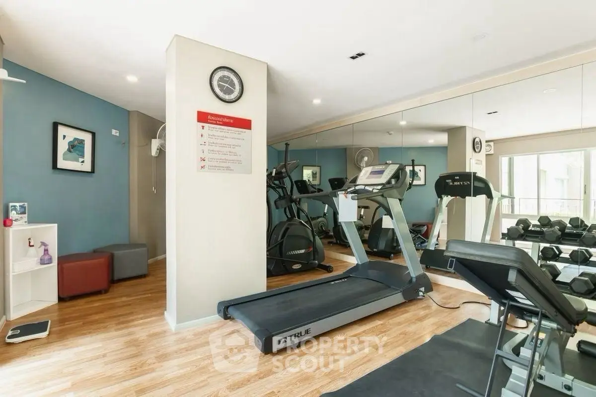 Modern gym with treadmill, weights, and mirrored wall in residential building.