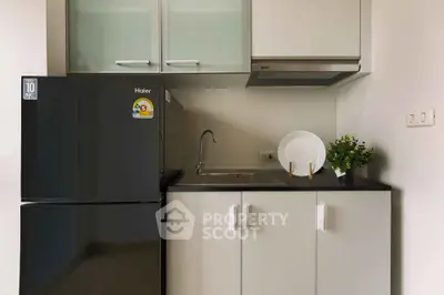 Modern compact kitchen with sleek cabinets and black fridge in a stylish apartment.
