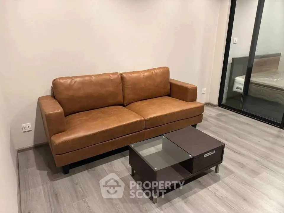 Modern living room with sleek leather sofa and glass-top coffee table on wooden flooring.