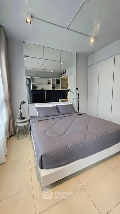 Modern bedroom with sleek design and mirrored wall, featuring a cozy bed and stylish lighting.
