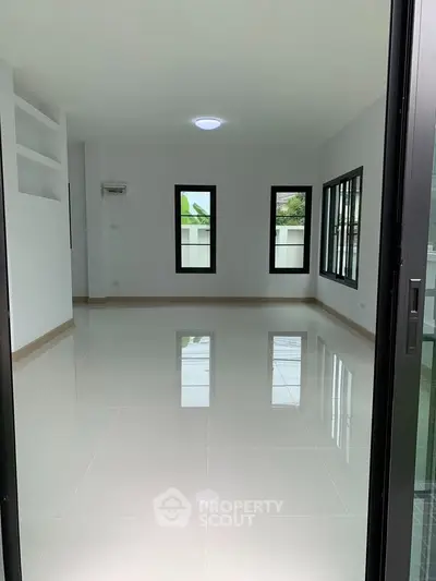 Spacious empty room with glossy tiled floors and large windows offering natural light.