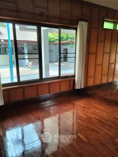 Spacious room with polished wooden floors and large window offering natural light.