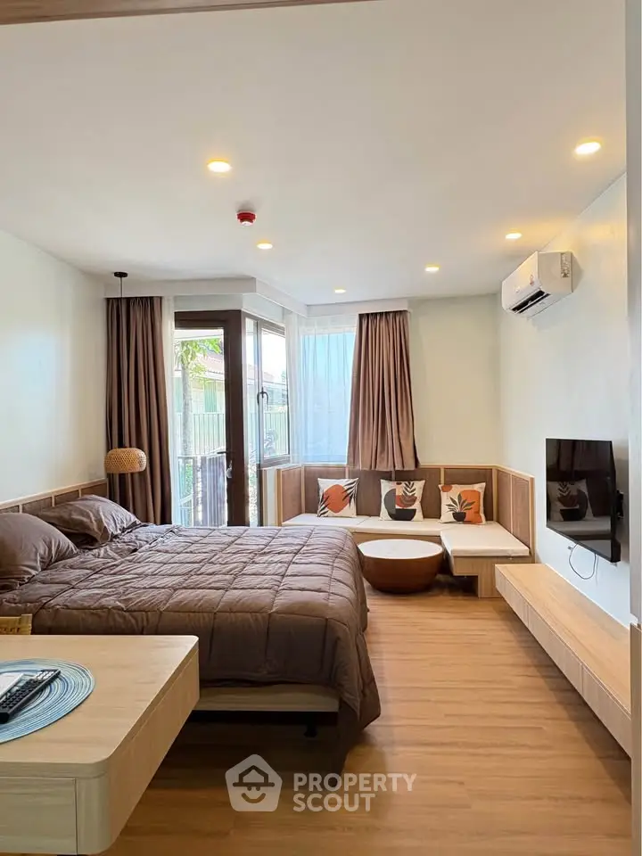 Modern bedroom with cozy decor and natural light, featuring a stylish bed and wall-mounted TV.