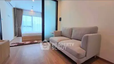 Modern living room with cozy sofa and view into a bright bedroom through sliding glass doors.