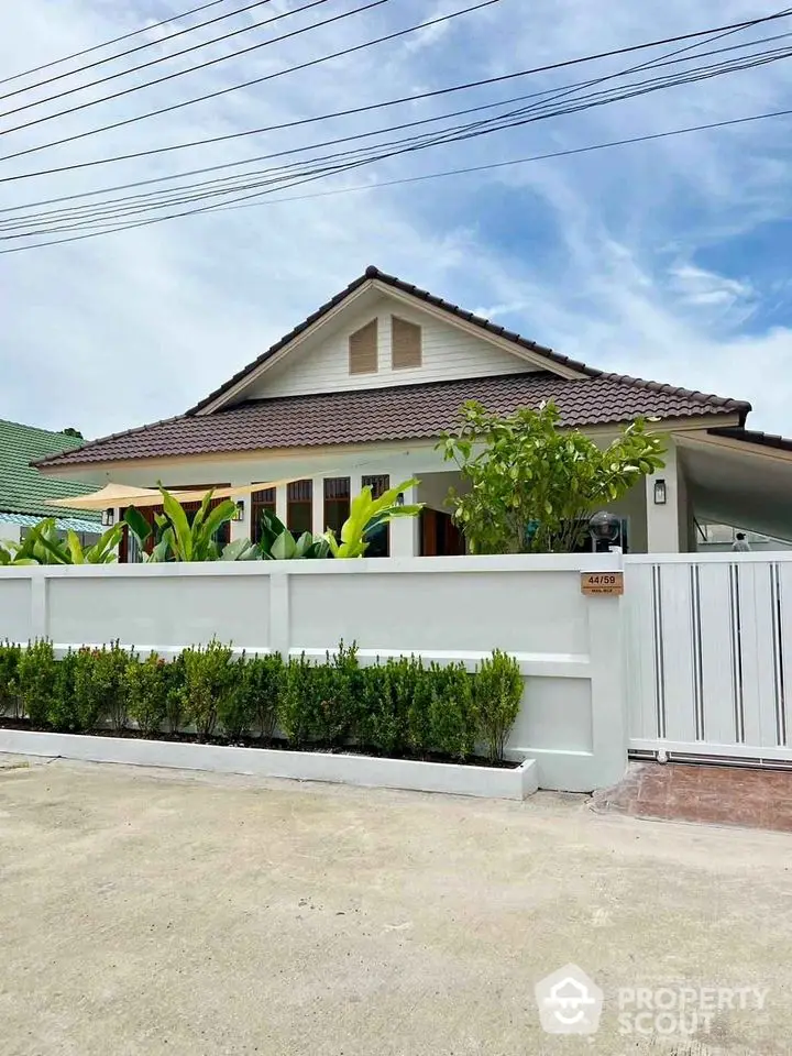 Charming suburban house with lush garden and modern fence under clear blue sky.