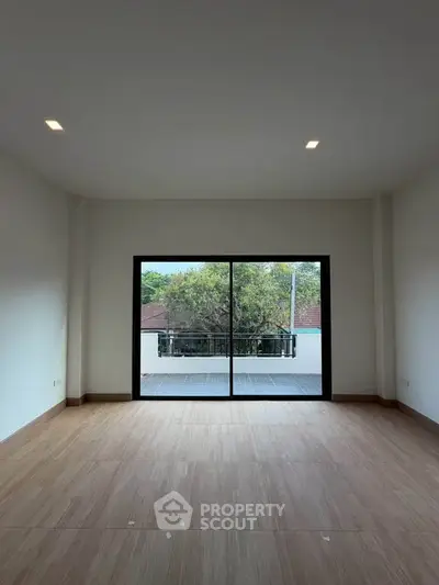 Spacious room with large sliding doors opening to a balcony with a view of trees.