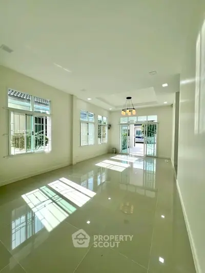 Spacious sunlit living room with glossy tiled floors and elegant chandelier