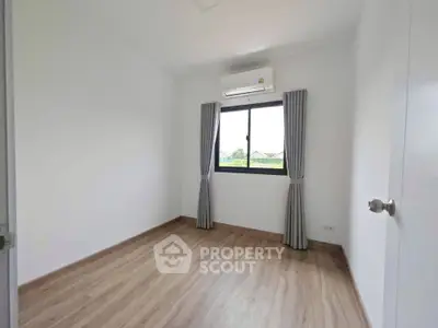 Spacious empty bedroom with wooden flooring and large window view.