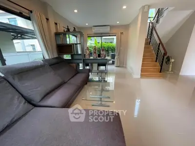Modern living room with sleek furniture and large windows offering garden view.