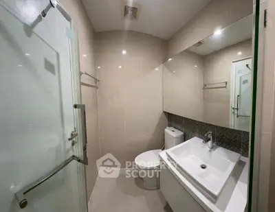 Modern bathroom with sleek fixtures and large mirror, featuring a glass shower enclosure and contemporary design.