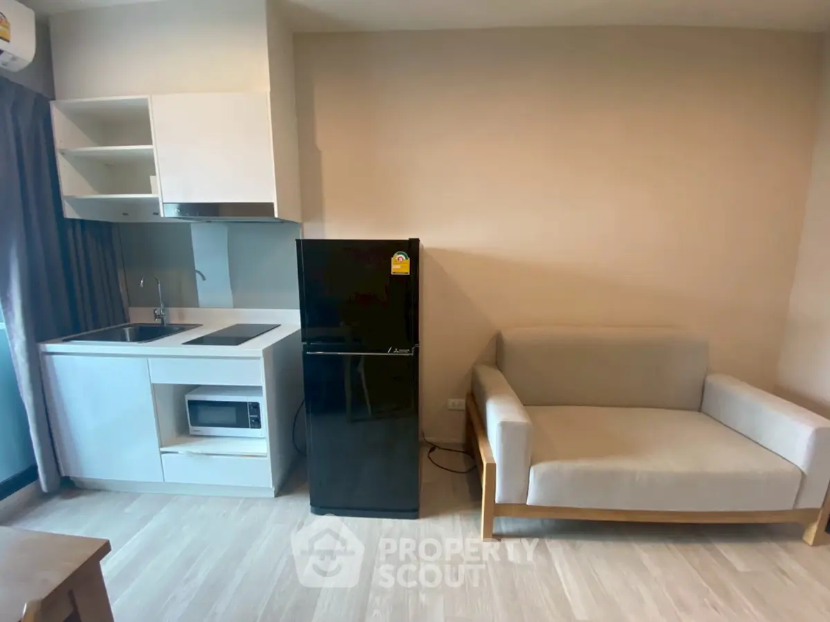 Modern compact living room with kitchenette, featuring sleek appliances and cozy seating.