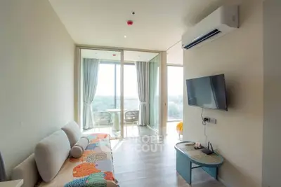 Modern living room with balcony view, featuring cozy sofa and wall-mounted TV in bright apartment.
