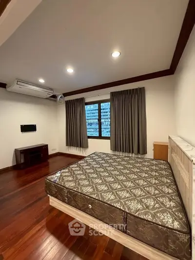Spacious bedroom with wooden flooring and large window in modern apartment.