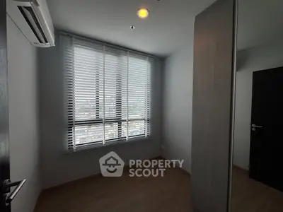Modern bedroom with large window and sleek blinds, featuring air conditioning and wooden flooring.