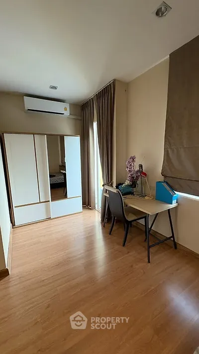Cozy bedroom with study area, featuring wooden flooring and air conditioning.