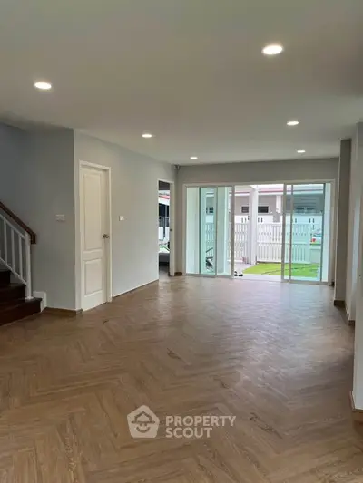 Spacious living room with wooden flooring and large windows opening to a garden view.