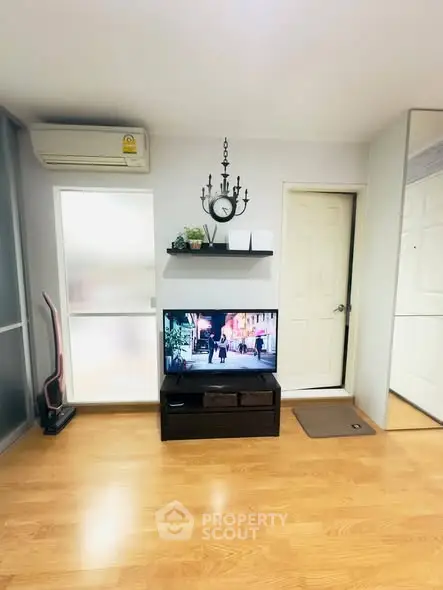 Modern living room with wooden flooring, TV setup, and air conditioning unit.