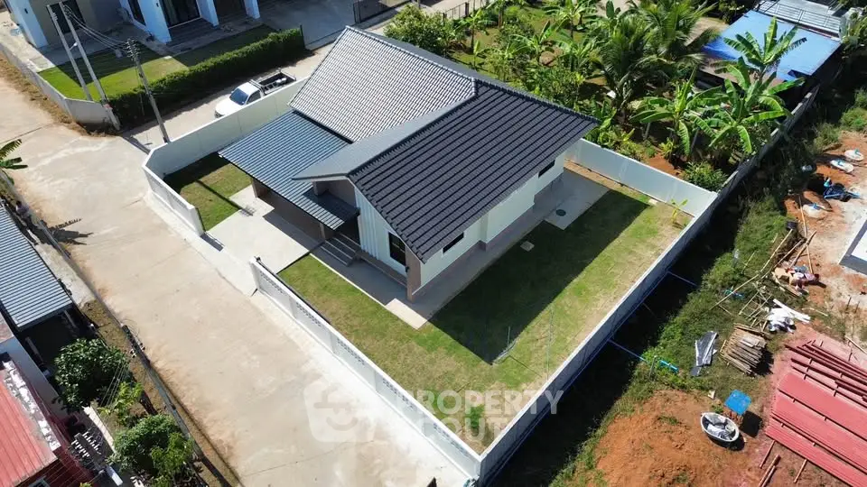 Aerial view of modern single-story house with spacious yard and sleek roof design.