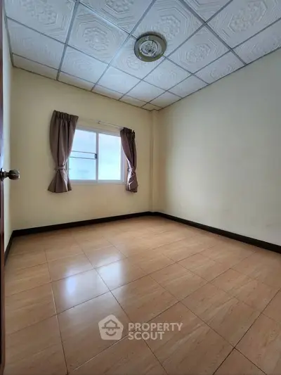 Spacious empty bedroom with tiled floor and window, ideal for customization.