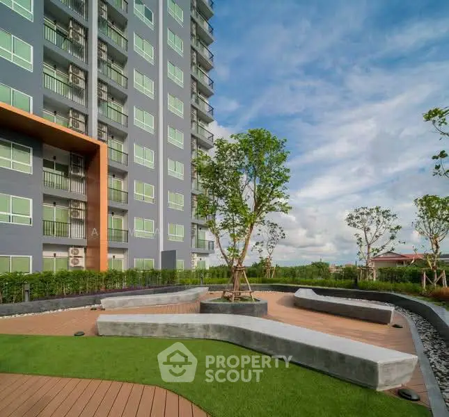 Modern apartment building with landscaped garden and seating area under a clear blue sky.