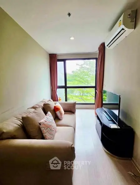Cozy living room with large window and modern furnishings, offering a serene view of greenery.