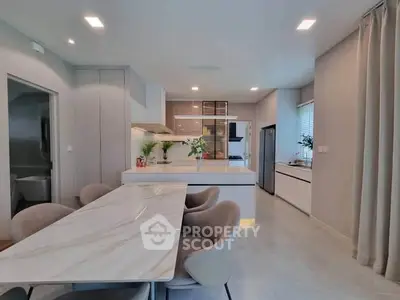 Modern kitchen with open layout and elegant dining area featuring marble table and plush chairs.