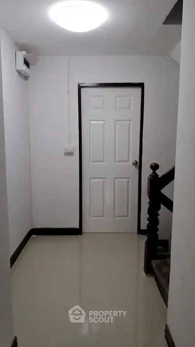 Minimalist hallway with white door and wooden staircase