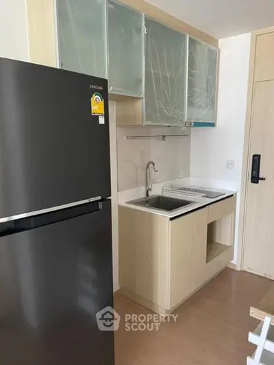 Modern compact kitchen with sleek fridge and minimalist cabinetry in a stylish apartment.