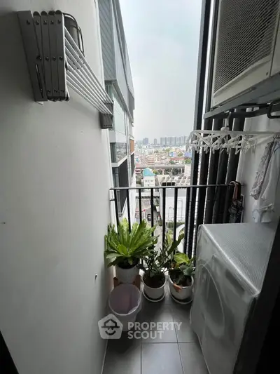Compact balcony with city view, laundry area, and potted plants in modern apartment.