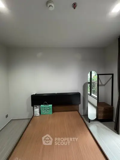 Modern bedroom with minimalist design featuring a wooden bed frame and large window for natural light.