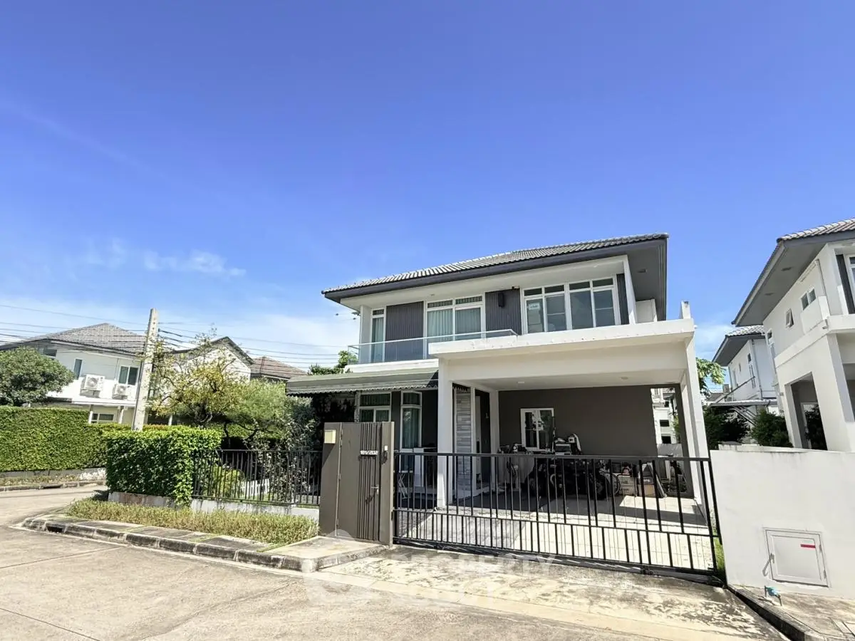 Modern two-story house with gated driveway and lush greenery under clear blue sky.