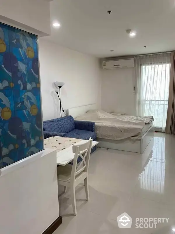 Bright and airy studio apartment with gleaming white tiles, modern furniture, and ample natural light from large windows, perfect for singles or couples.