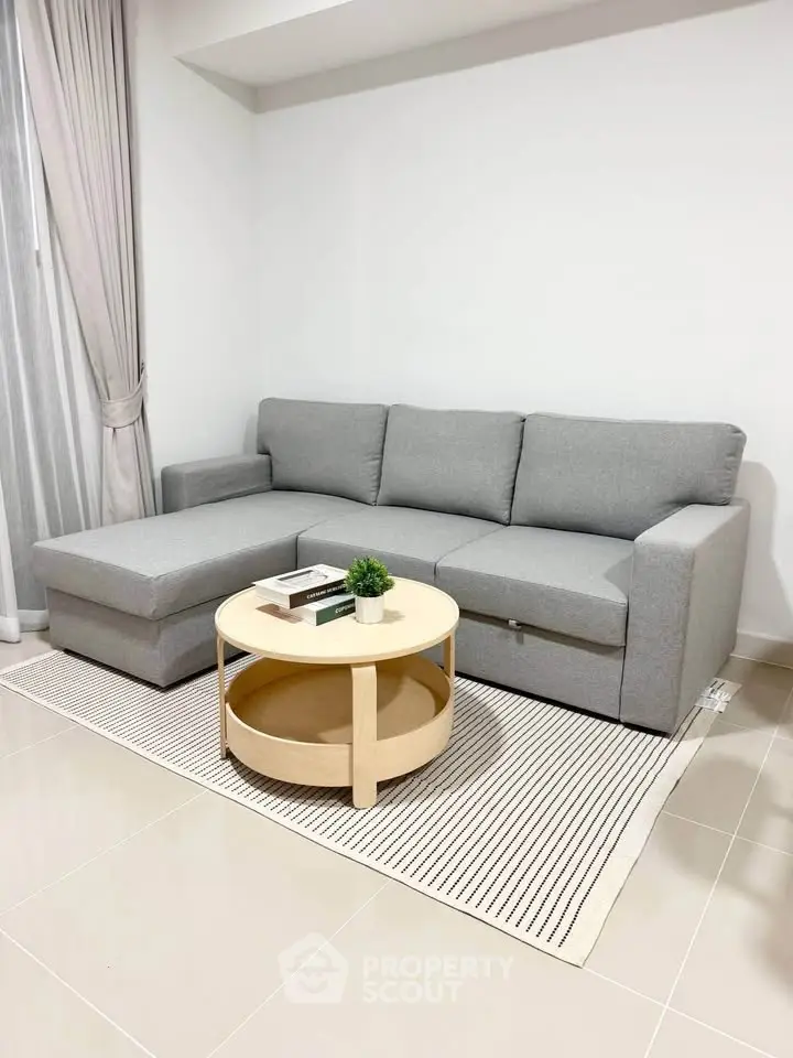 Modern living room with gray sectional sofa and round wooden coffee table on striped rug.