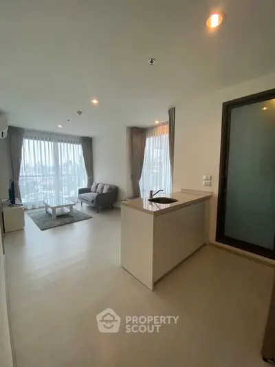 Modern open-layout living room with kitchen island and large windows offering city views.