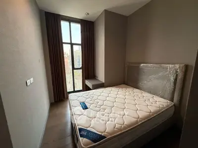 Cozy bedroom with large window and city view, featuring a new mattress and elegant decor.