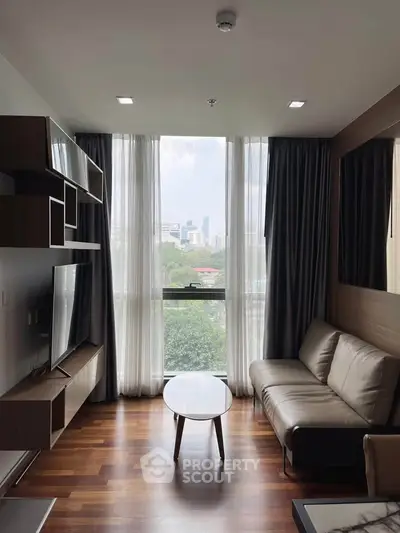 Modern living room with large window and city view, featuring sleek furniture and wooden flooring.