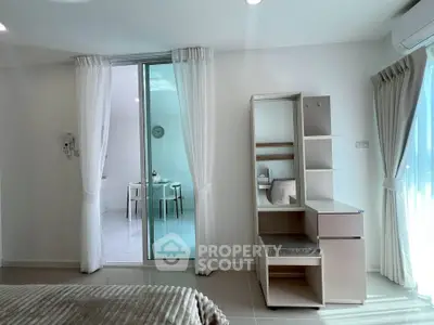 Modern bedroom with sleek furniture and natural light, featuring a view into a stylish dining area.