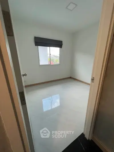 Spacious empty bedroom with large window and glossy white floor tiles.